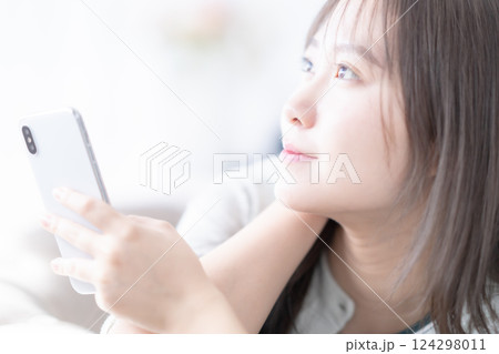 寝転んでリラックスしながらスマホを見る若い女性 寝転んでリラックスしながらスマホを見る若い女性 124298011