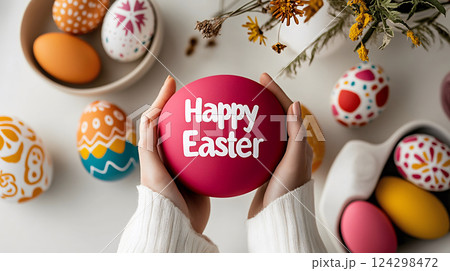 Happy Easter, hands holding a festive pink egg with white lettering, surrounded by colorful eggs 124298472