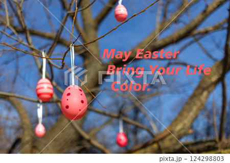 Decorative pink Easter eggs hang from tree branches against blue sky background with fun holiday message Decorative pink Easter eggs hang from tree branches against blue sky background with fun holiday message 124298803