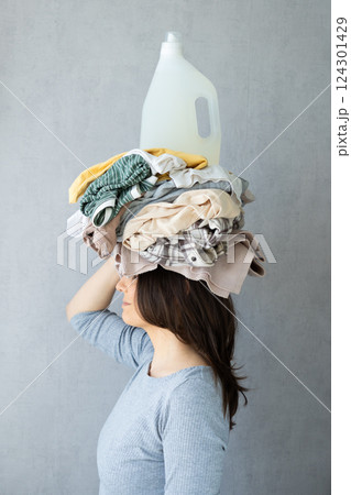 washing clothes, woman holds stack of clothes on head and conditioner laundry after dry cleaning. washing clothes, woman holds stack of clothes on head and conditioner laundry after dry cleaning. 124301429