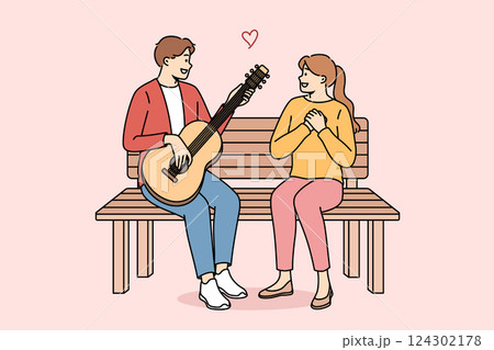 Man sings romantic serenade to woman and plays guitar, sitting on bench during date in park 124302178
