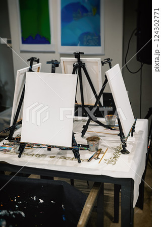 Easels in a Studio, art school for adults. Wooden Easels With Canvas, Art supplies on table near easel with canvas indoors. Painting Lessons in artist studio 124302771