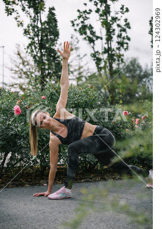 Woman practicing outdoor fitness routine among blooming rose bushes in a park during daytime 124302969