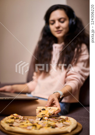 smiling woman working on laptop computer and eating pizza at home, focus on pizza smiling woman working on laptop computer and eating pizza at home, focus on pizza 124306220