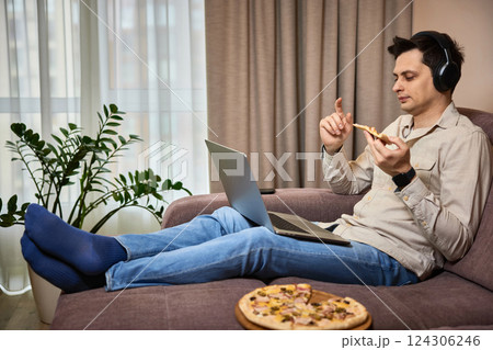 man sitting on sofa and eating pizza while working on laptop man sitting on sofa and eating pizza while working on laptop 124306246