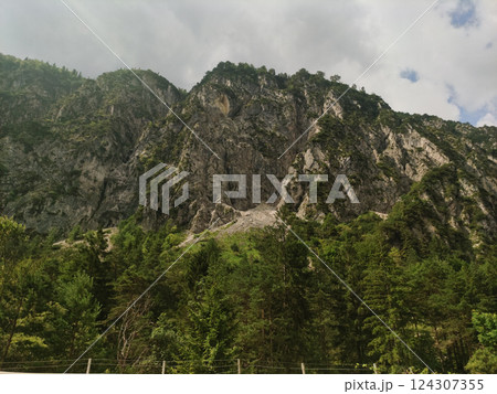 Rugged alpine cliffs rising above pine forest, clouded peaks casting moody atmosphere over dramatic rocky wilderness in italian mountain terrain 124307355