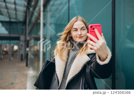 Happy blonde Woman makes selfie mobile photo on modern urban background. Charming female wearing stylish outfit have fine. High quality photo. 124308166