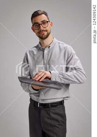 Young man in office wear opening laptop with soft smile, engaged in task. Young man in office wear opening laptop with soft smile, engaged in task. 124309142