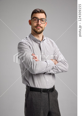 Portrait of young serious businessman wearing shirt and black pants, looking with precise against grey studio background Portrait of young serious businessman wearing shirt and black pants, looking with precise against grey studio background 124309155