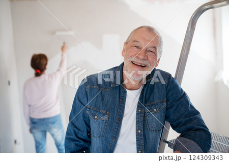 Senior man painting walls in new home, looking at camera. 124309343