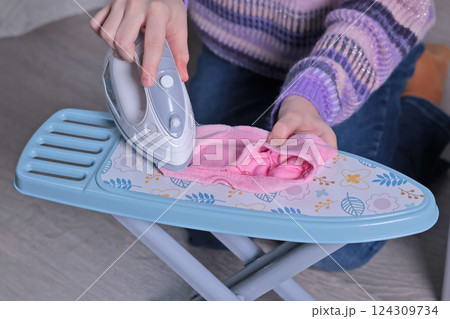 Girl play with toy iron and washing machine at home on floor. Cleaning, household chores, kids and educational games. Girl play with toy iron and washing machine at home on floor. Cleaning, household chores, kids and educational games. 124309734