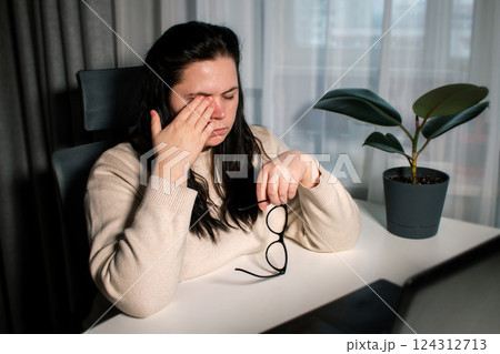 Tired woman working at home with laptop holding eyeglasses rubbing eyes and feeling fatigue. Stress and frustration concept. Tired eyes Tired woman working at home with laptop holding eyeglasses rubbing eyes and feeling fatigue. Stress and frustration concept. Tired eyes 124312713