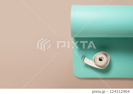 Green yoga mat and white strap on beige background. Relaxation and meditation concept. Accessories for yoga practice. Top view. Copy space. 124312904