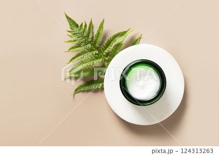Open jar of cosmetic cream decorated fern leaf. Beauty anti ageing cream, body lotion, moisturizer texture of natural cosmetics on nude beige background. Copy space. Open jar of cosmetic cream decorated fern leaf. Beauty anti ageing cream, body lotion, moisturizer texture of natural cosmetics on nude beige background. Copy space. 124313263