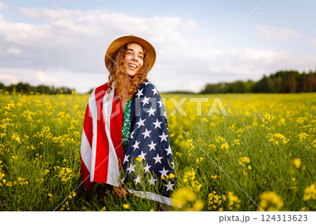 Young woman with american flag on blooming meadow. Independence Day. USA flag fluttering in the wind 124313623