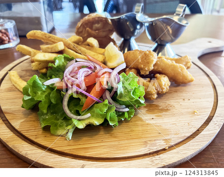 fish and chips on a wooden tray with sauces and fresh vegetables on a table in a cafe fish and chips on a wooden tray with sauces and fresh vegetables on a table in a cafe 124313845
