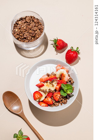 Greek yogurt with chocolate granola, strawberries and banana in a bowl on a beige background 124314161