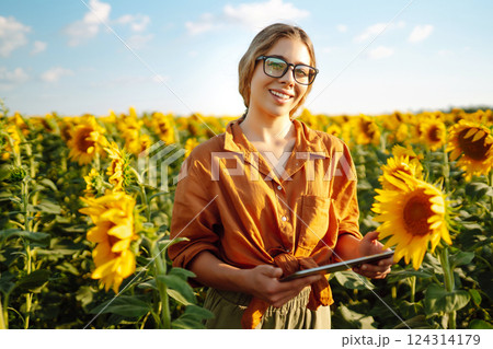Female farmer analyzing sunflower on sunny day. Agriculture and harvesting concept. 124314179