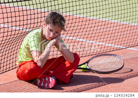 The boy lost the tennis competition. The child sits at the net with a racket. Psychology of sports in childhood. 124314284
