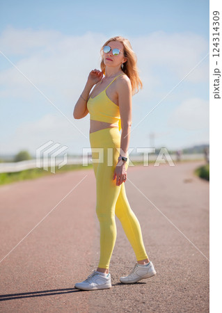 A woman in a yellow sports outfit walks along the road. She's going for a run. A woman in a yellow sports outfit walks along the road. She's going for a run. 124314309
