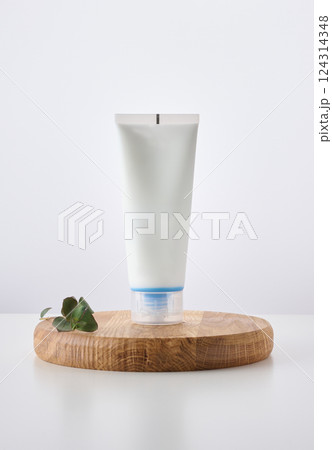 White cosmetic tube with cap placed on a round wooden stand, accompanied by eucalyptus leaves. White cosmetic tube with cap placed on a round wooden stand, accompanied by eucalyptus leaves. 124314348