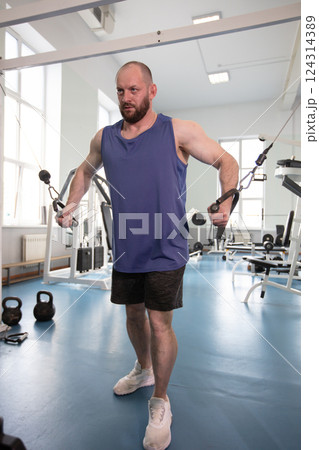 Male athlete bodybuilder exercising in the gym. Strength training on a cable machine. Male athlete bodybuilder exercising in the gym. Strength training on a cable machine. 124314389