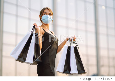 Beautiful woman in protective sterile medical mask with shopping bags near shopping center.Covid- 2019. Beautiful woman in protective sterile medical mask with shopping bags near shopping center.Covid- 2019. 124314407
