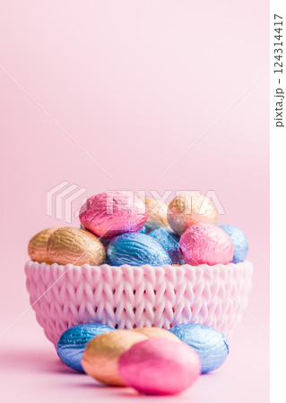 Chocolate easter eggs wrapped in multi colored foil in bowl on pink background. 124314417