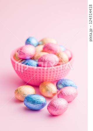 Chocolate easter eggs wrapped in multi colored foil in bowl on pink background. 124314418
