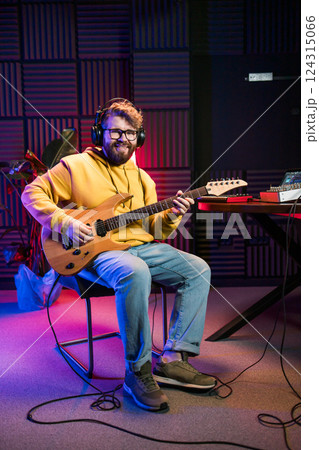 Male singer playing guitar and singing a song. Man performing in a recording studio. Recording music album. 124315066