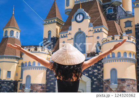 woman tourist traveler in a Vietnamese hat Non La on at castle on Vinpearl Island at VinWonders Amusement Park in Nha Trang at summer vacation in Asia. Travel and tourism in Vietnam 124320362
