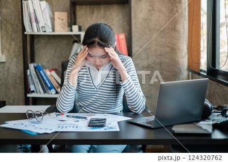 Young woman feeling stressed while reviewing financial documents at her office desk with a laptop. Young woman feeling stressed while reviewing financial documents at her office desk with a laptop. 124320762