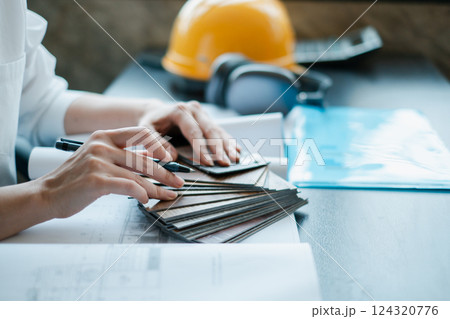 Hands of a professional examining material samples and blueprints in an office setting, with a hard hat and headphones nearby. Hands of a professional examining material samples and blueprints in an office setting, with a hard hat and headphones nearby. 124320776
