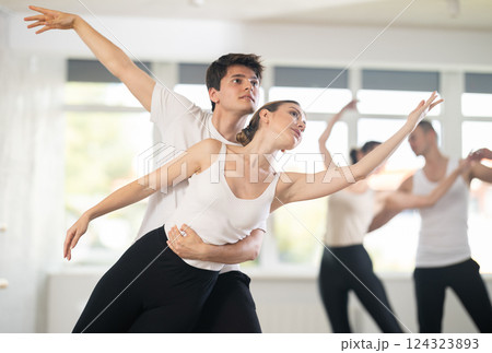 Portrait of positive young man and female partner training ballet pose with group of guys and girls in dance class 124323893