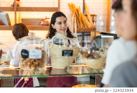 Seller in an apron is standing in a coffee shop and talking to a client 124323934