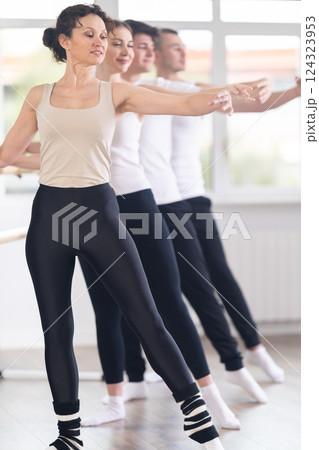 Woman performing demi rond at ballet barre in group studio Woman performing demi rond at ballet barre in group studio 124323953
