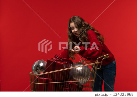 Young girl in red sweater reaches into gold shopping cart 124323969