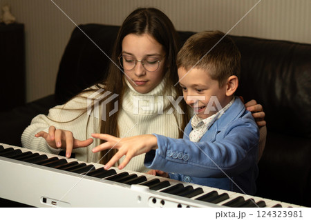 Young boy playing piano with teen girl mentor 124323981