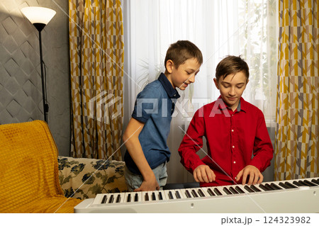 Two boys playing the piano together in cozy home setting Two boys playing the piano together in cozy home setting 124323982