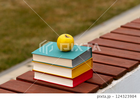 Stack of colorful hardcover books with apple on bench. Stack of colorful hardcover books with apple on bench. 124323984