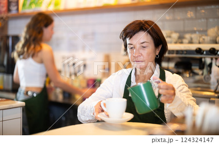 Senior woman cafe worker pours coffee from cezve coffee pot into cup 124324147