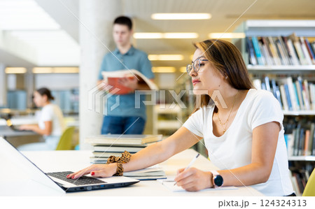 Portrait of adult latino woman studying at library using books and laptop 124324313