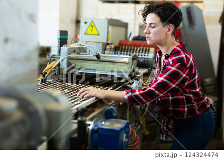 Skilled farmer woman working with automatic filling and seeding line for growing containerized seedlings of decorative plants in greenhouse 124324474