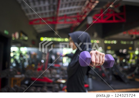 Arab middle eastern muslim woman working out while lifting a dumbbell at the gym. Fitness exercise and healthy lifestyle concept Arab middle eastern muslim woman working out while lifting a dumbbell at the gym. Fitness exercise and healthy lifestyle concept 124325724