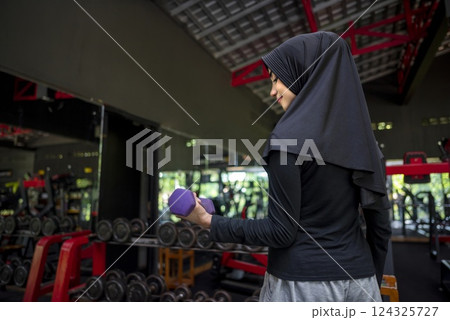Arab middle eastern muslim woman working out while lifting a dumbbell at the gym. Fitness exercise and healthy lifestyle concept Arab middle eastern muslim woman working out while lifting a dumbbell at the gym. Fitness exercise and healthy lifestyle concept 124325727