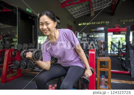 Chinese east asian woman working out while lifting a dumbbell at the gym. Fitness exercise and healthy lifestyle concept Chinese east asian woman working out while lifting a dumbbell at the gym. Fitness exercise and healthy lifestyle concept 124325728