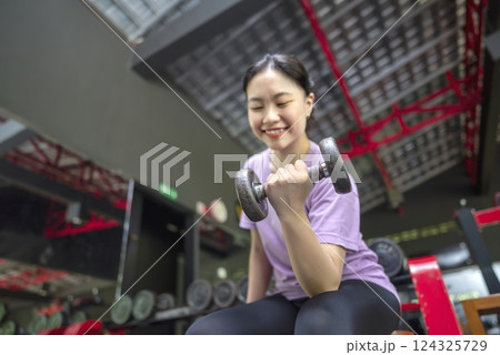Chinese east asian woman working out while lifting a dumbbell at the gym. Fitness exercise and healthy lifestyle concept 124325729