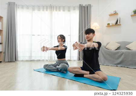Two Asian Young Adults Practicing Yoga Poses Together in Bright and Cozy Living Room at Home, Focusing on Stretching and Wellness Activities 124325930
