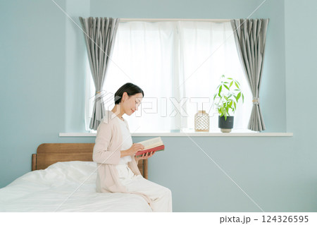 ベッドのそばに座って本を読む女性 124326595