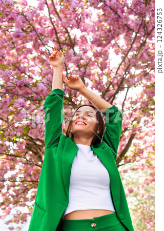 Happy woman enjoys nature under a full bloom cherry tree Happy woman enjoys nature under a full bloom cherry tree 124326753